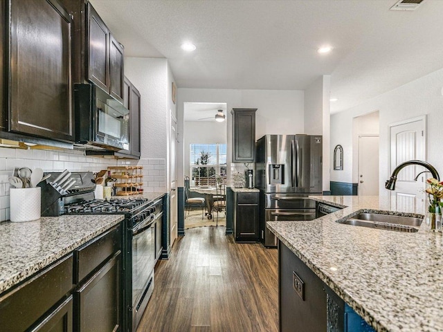 kitchen featuring dark wood-style floors, a sink, light stone countertops, decorative backsplash, and black appliances