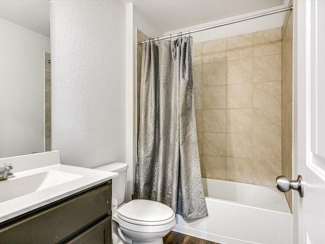 bathroom featuring a textured wall, shower / bath combo with shower curtain, vanity, and toilet