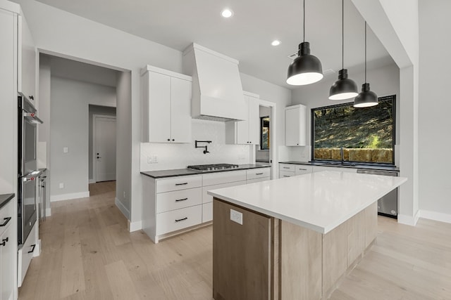 kitchen with a center island, white cabinets, custom exhaust hood, light hardwood / wood-style flooring, and decorative light fixtures