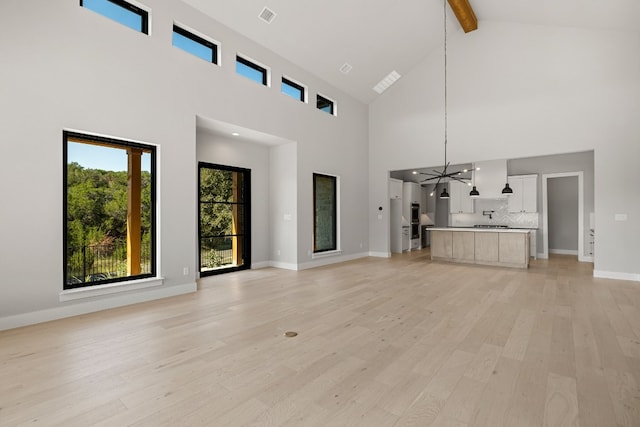 unfurnished living room with light hardwood / wood-style floors, beam ceiling, an inviting chandelier, and high vaulted ceiling