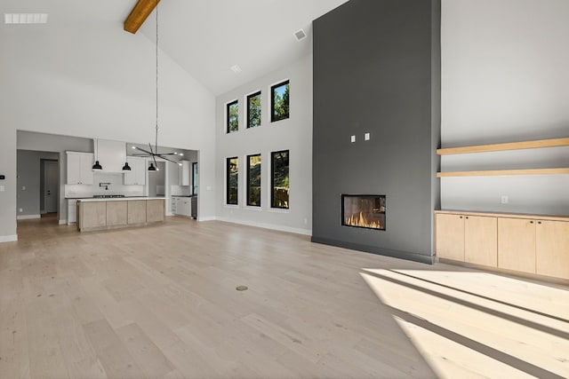 unfurnished living room with beamed ceiling, an inviting chandelier, light hardwood / wood-style flooring, and high vaulted ceiling