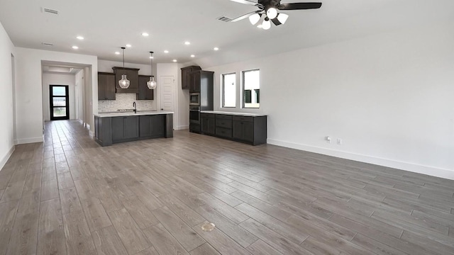 kitchen with dark brown cabinetry, backsplash, hardwood / wood-style flooring, and a center island with sink