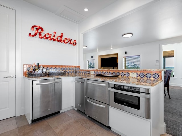 kitchen with decorative backsplash, white cabinets, kitchen peninsula, light tile patterned floors, and stainless steel appliances