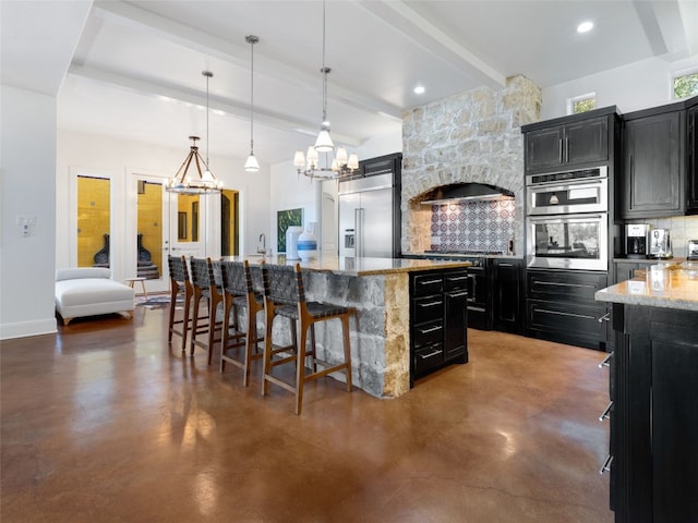 kitchen featuring appliances with stainless steel finishes, decorative backsplash, hanging light fixtures, an island with sink, and a kitchen bar