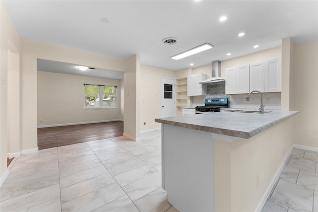 kitchen with wall chimney range hood, light hardwood / wood-style flooring, backsplash, black gas range oven, and white cabinetry