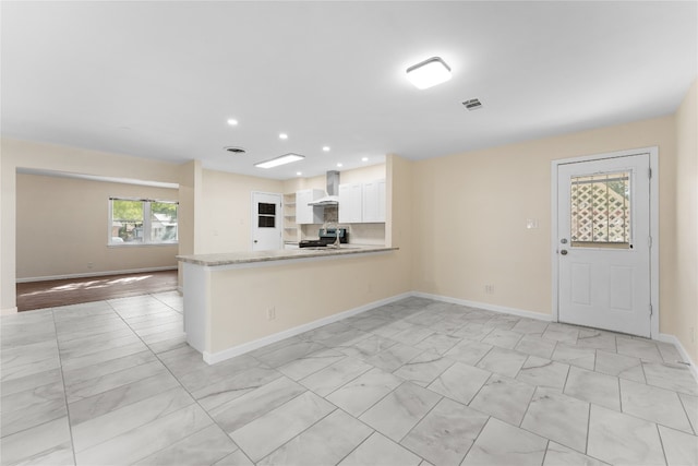 kitchen featuring kitchen peninsula, white cabinetry, wall chimney exhaust hood, stainless steel stove, and light stone counters