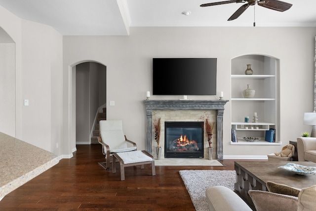 living room featuring crown molding, ceiling fan, dark hardwood / wood-style floors, and built in features