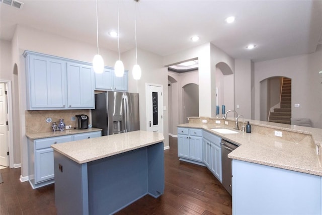 kitchen featuring appliances with stainless steel finishes, an island with sink, sink, hanging light fixtures, and light stone counters