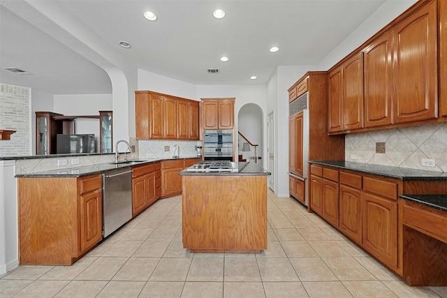 kitchen with sink, kitchen peninsula, a kitchen island, backsplash, and appliances with stainless steel finishes