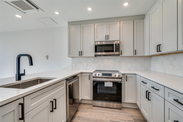 kitchen with sink, stainless steel appliances, backsplash, and light hardwood / wood-style floors