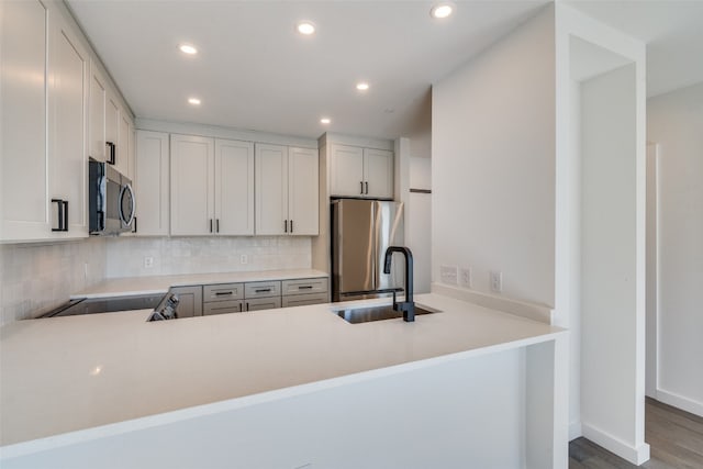 kitchen with wood-type flooring, kitchen peninsula, appliances with stainless steel finishes, and sink