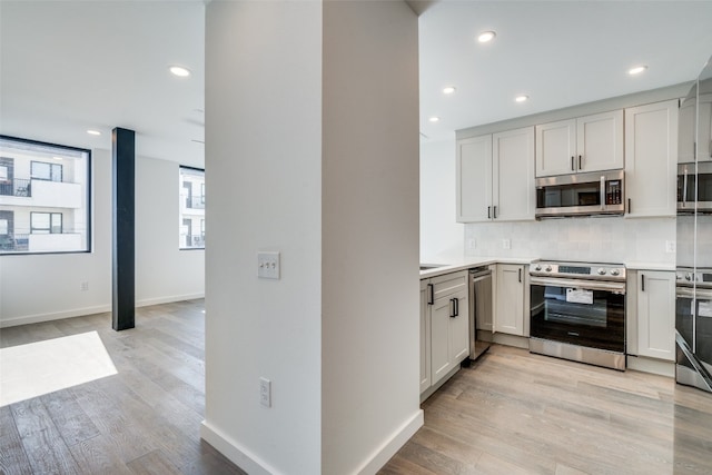 kitchen featuring decorative backsplash, stainless steel appliances, white cabinets, and light hardwood / wood-style floors