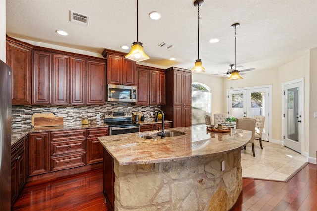 kitchen featuring french doors, sink, dark hardwood / wood-style floors, a kitchen island with sink, and appliances with stainless steel finishes