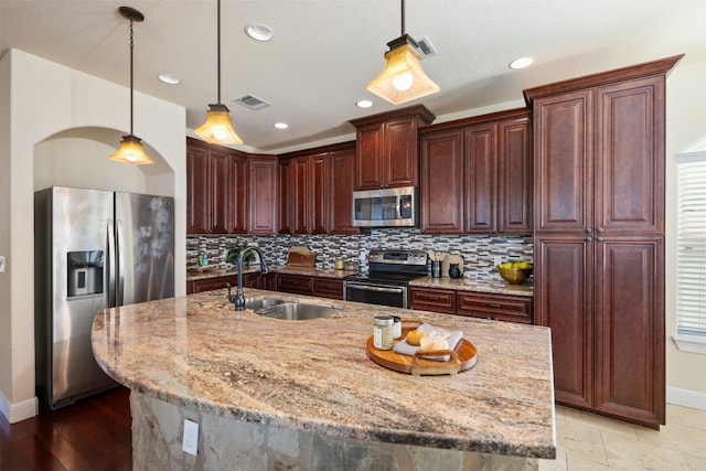 kitchen featuring light stone countertops, sink, appliances with stainless steel finishes, and an island with sink