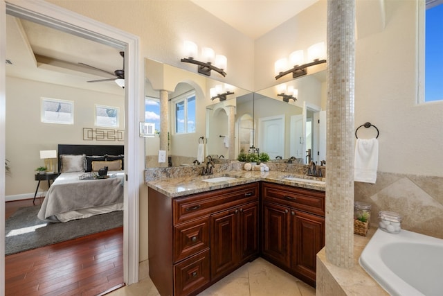 bathroom with hardwood / wood-style flooring, ceiling fan, vanity, and tiled bath