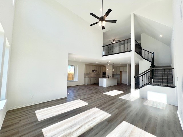 unfurnished living room with ceiling fan, dark hardwood / wood-style flooring, a towering ceiling, and sink