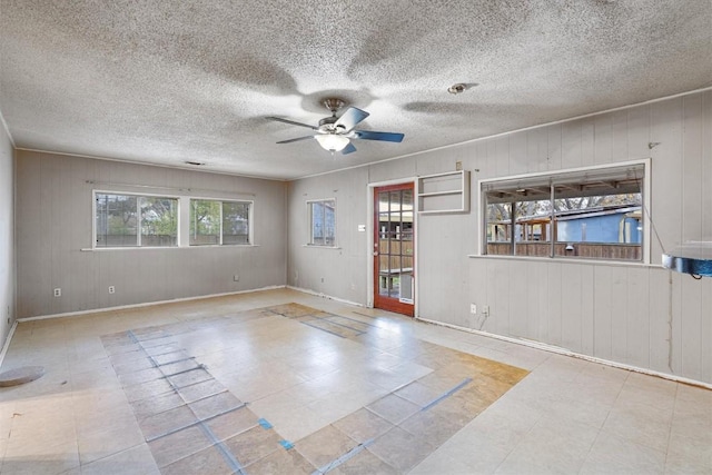 unfurnished room with a textured ceiling, ceiling fan, and wood walls