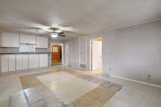 kitchen featuring wooden walls, white cabinets, a textured ceiling, and ceiling fan