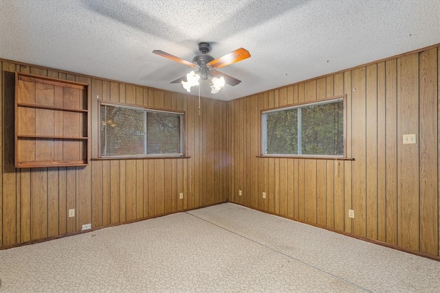 spare room with ceiling fan, wood walls, and a textured ceiling