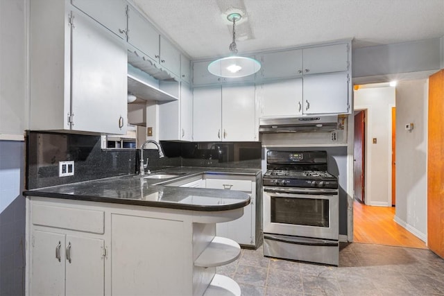 kitchen with sink, hanging light fixtures, stainless steel gas range oven, kitchen peninsula, and a textured ceiling