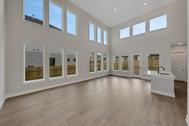 unfurnished living room with a towering ceiling, light hardwood / wood-style flooring, and sink