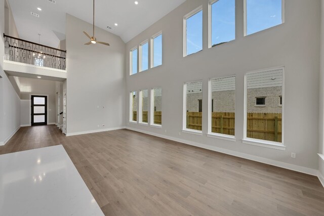 unfurnished living room featuring ceiling fan, hardwood / wood-style floors, and a towering ceiling