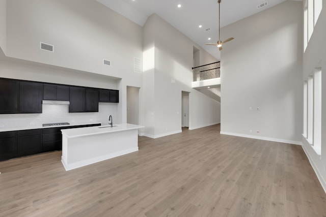 kitchen with an island with sink, gas cooktop, and a towering ceiling