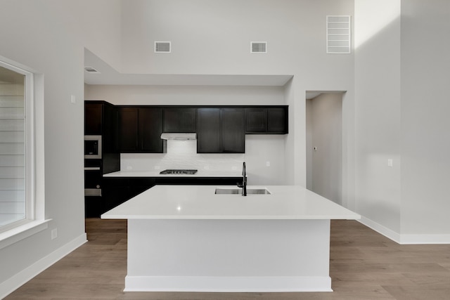 kitchen featuring a kitchen island with sink, light hardwood / wood-style floors, stainless steel microwave, sink, and black gas stovetop