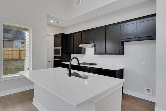 kitchen with sink, hardwood / wood-style floors, tasteful backsplash, a center island with sink, and appliances with stainless steel finishes