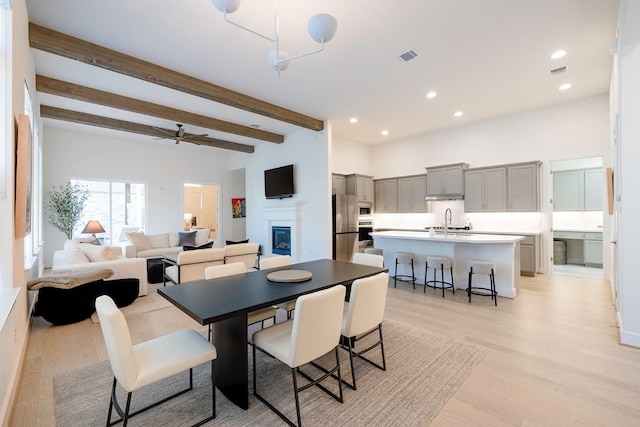 dining room with ceiling fan, beamed ceiling, light hardwood / wood-style flooring, and sink