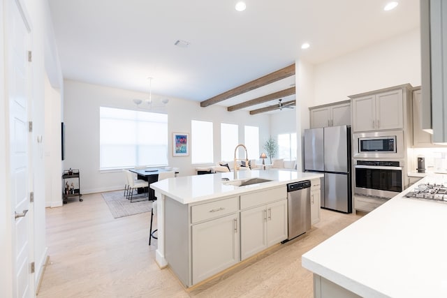 kitchen featuring sink, an island with sink, beam ceiling, light hardwood / wood-style flooring, and appliances with stainless steel finishes