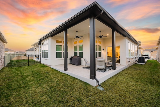 back house at dusk featuring ceiling fan, a yard, a patio, and central AC