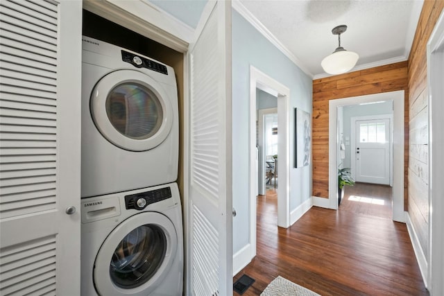 laundry room featuring dark hardwood / wood-style flooring, a textured ceiling, stacked washer / dryer, wooden walls, and crown molding