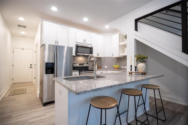 kitchen featuring white cabinets, kitchen peninsula, stainless steel appliances, light stone countertops, and light wood-type flooring