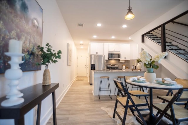 kitchen with appliances with stainless steel finishes, tasteful backsplash, white cabinetry, hanging light fixtures, and light hardwood / wood-style flooring