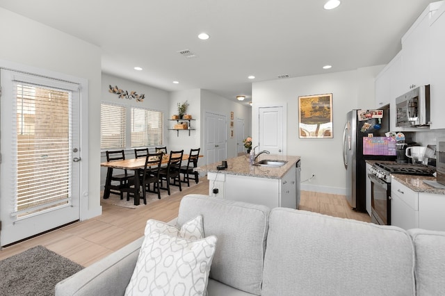 kitchen featuring light hardwood / wood-style floors, white cabinets, stainless steel appliances, a center island with sink, and light stone countertops