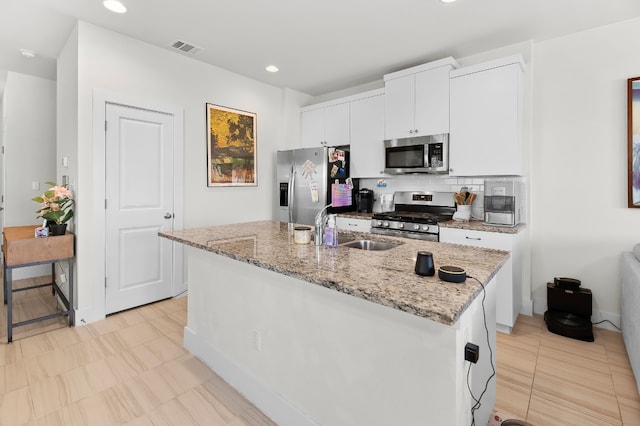 kitchen with appliances with stainless steel finishes, decorative backsplash, white cabinets, a kitchen island with sink, and sink