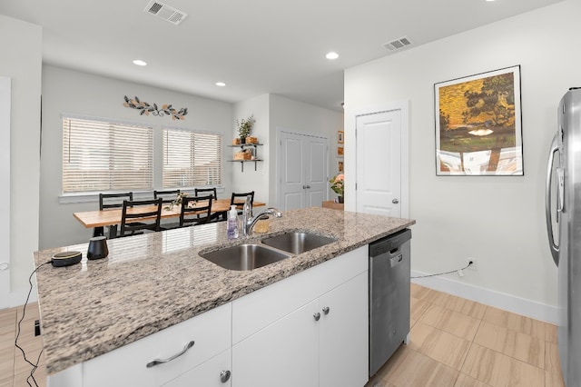 kitchen with sink, white cabinetry, a center island with sink, appliances with stainless steel finishes, and light stone countertops