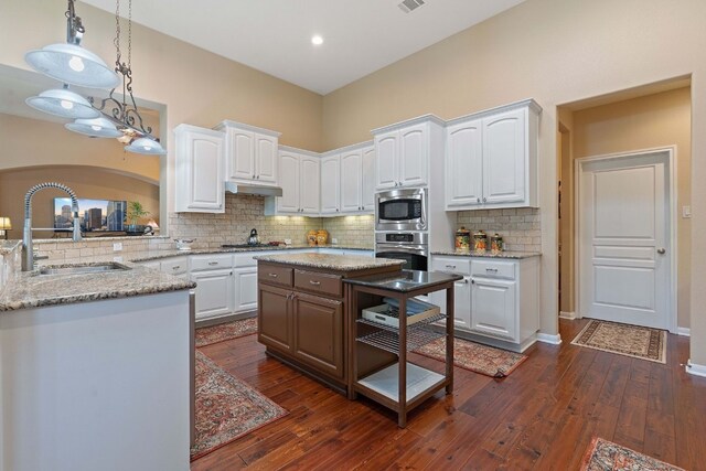 kitchen with hanging light fixtures, dark wood-type flooring, white cabinetry, appliances with stainless steel finishes, and decorative backsplash