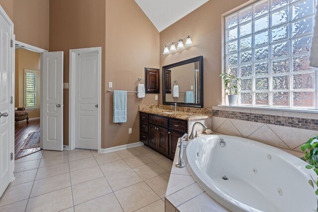 bathroom with tile patterned flooring, vanity, high vaulted ceiling, and a relaxing tiled tub