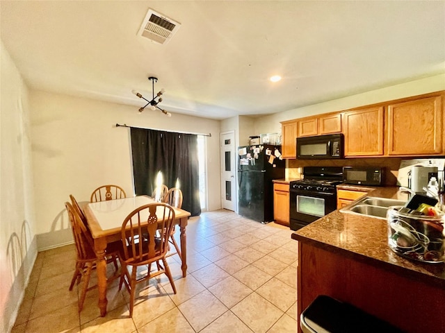 kitchen with dark stone countertops, black appliances, light tile patterned floors, and sink