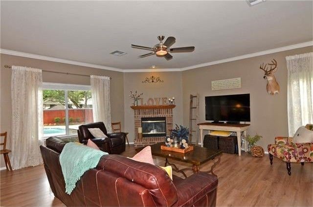 living room featuring ornamental molding, ceiling fan, light hardwood / wood-style floors, and a fireplace