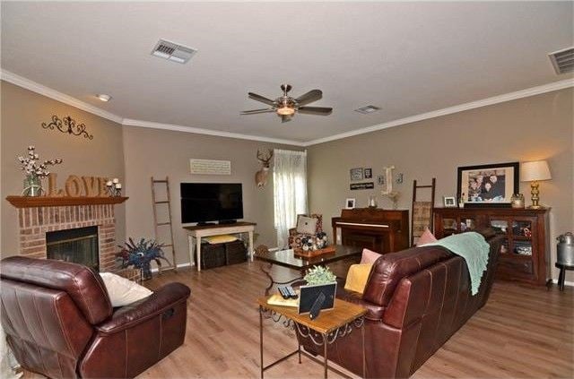 living room featuring a brick fireplace, light wood-type flooring, ceiling fan, and crown molding