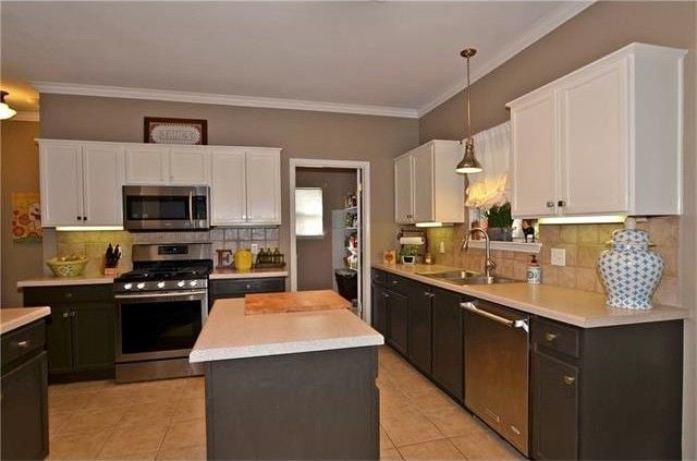 kitchen featuring sink, white cabinets, hanging light fixtures, a kitchen island, and appliances with stainless steel finishes