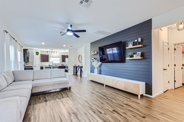 living room with light wood-type flooring, ceiling fan, and wood walls