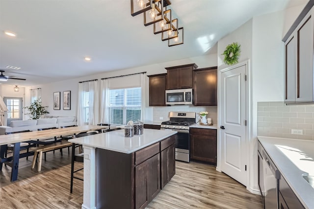 kitchen featuring dark brown cabinets, open floor plan, light wood finished floors, and stainless steel appliances