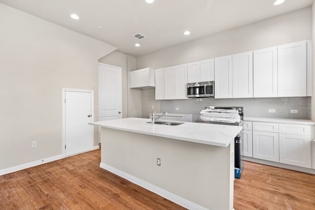 kitchen with light wood-type flooring, a kitchen island with sink, sink, and white cabinets