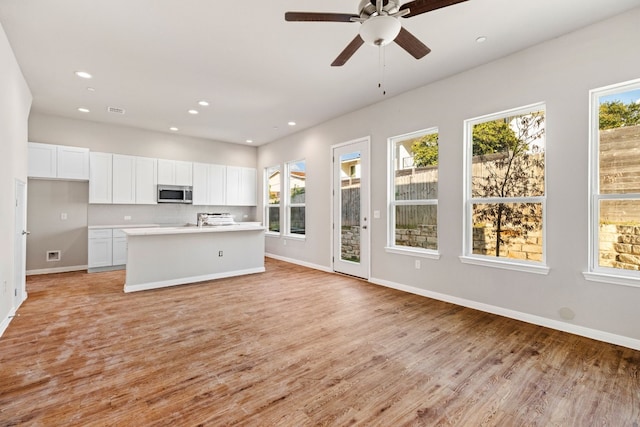 kitchen with light hardwood / wood-style floors, white cabinets, a kitchen island with sink, and ceiling fan