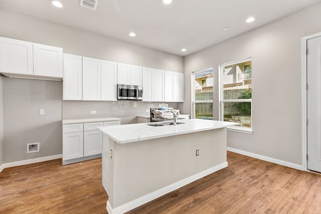 kitchen with an island with sink, sink, light hardwood / wood-style floors, and white cabinets