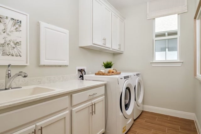 washroom with washing machine and dryer, cabinets, sink, and light hardwood / wood-style flooring